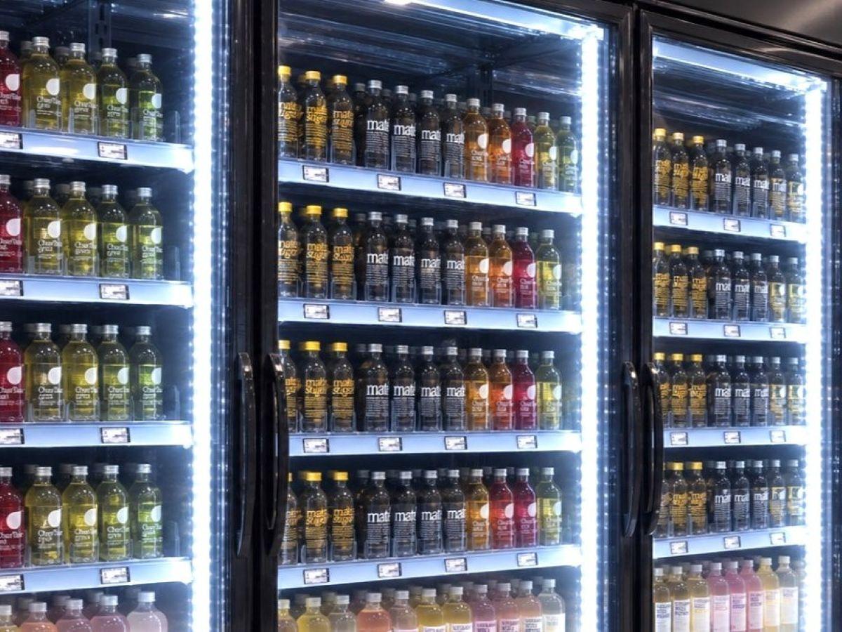 Glass bottles held front-facing by POS-T SuperVario SloMo pushers in a lit glass-door cooler